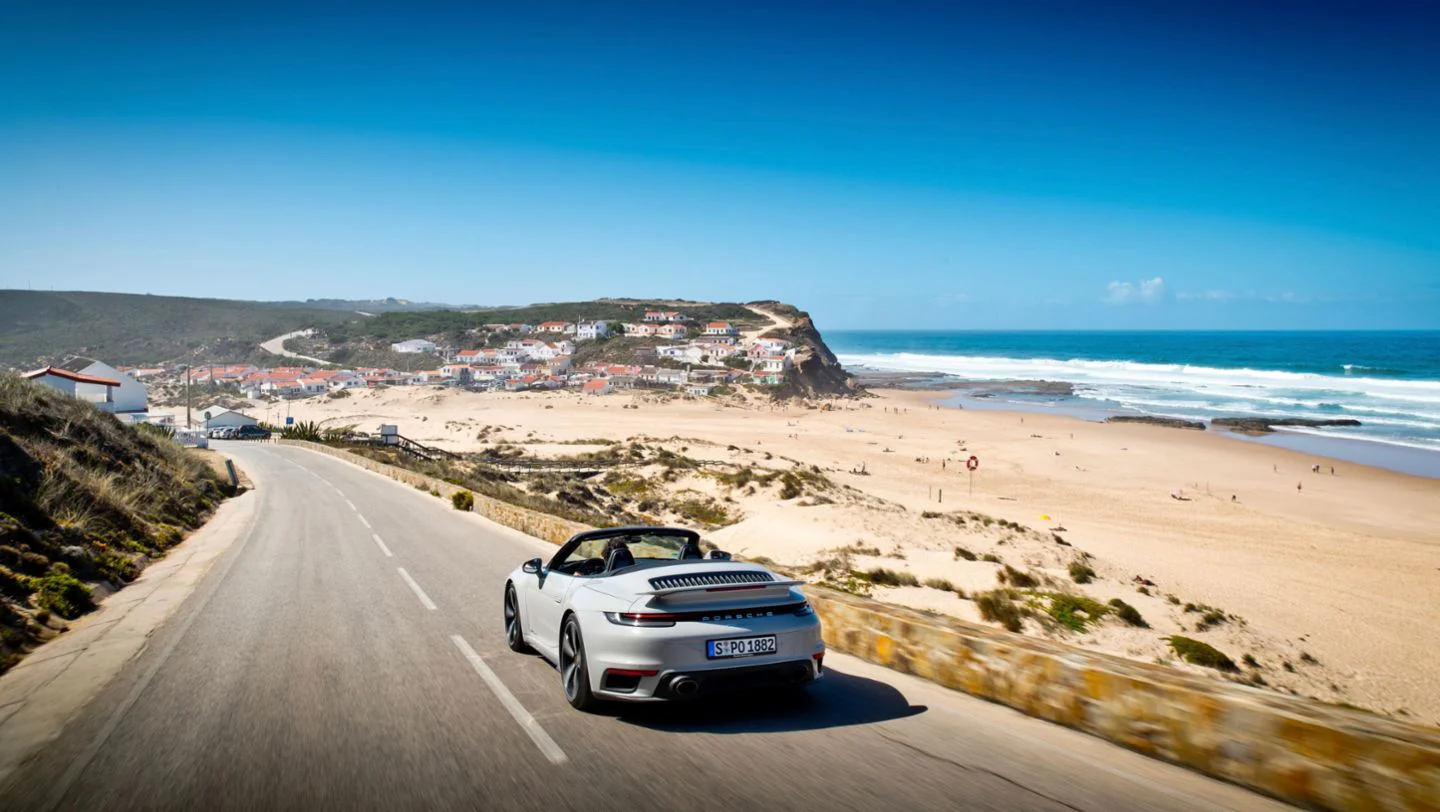 White Porsche on a coastal road above a beach
