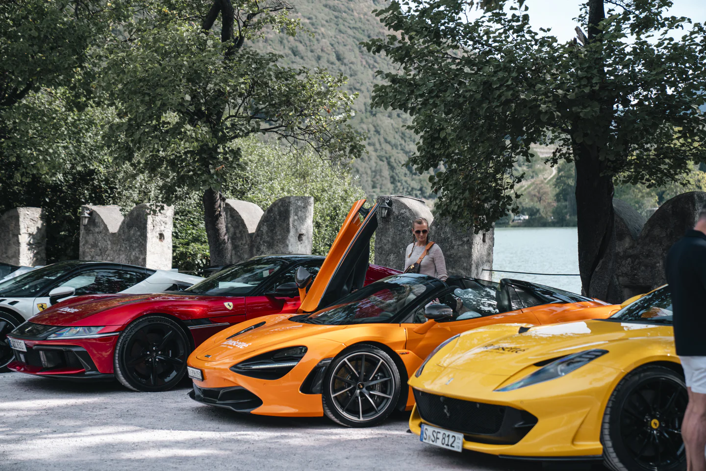 Red Ferrari, orange McLaren with its door raised and yellow Ferrari lined up beside a lake